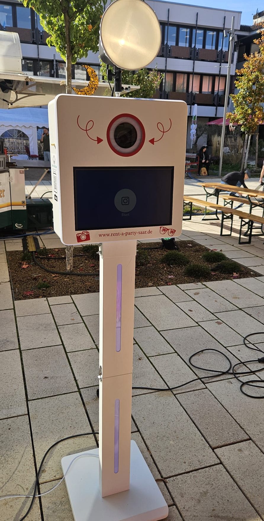 Fotobox mit Bildschirm und Kamera auf einem Standfuß im Freien.