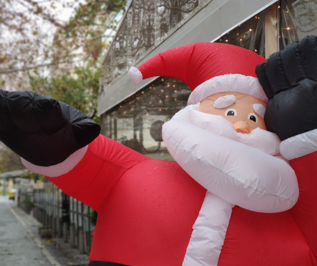 Aufblasbarer Santa Claus winkt fröhlich in einer festlich geschmückten Umgebung.