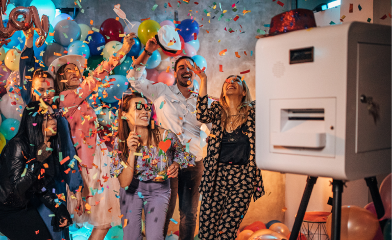 Gruppenevent mit bunten Luftballons, Konfetti und fröhlichen Menschen, die feiern vor einer Fotobox